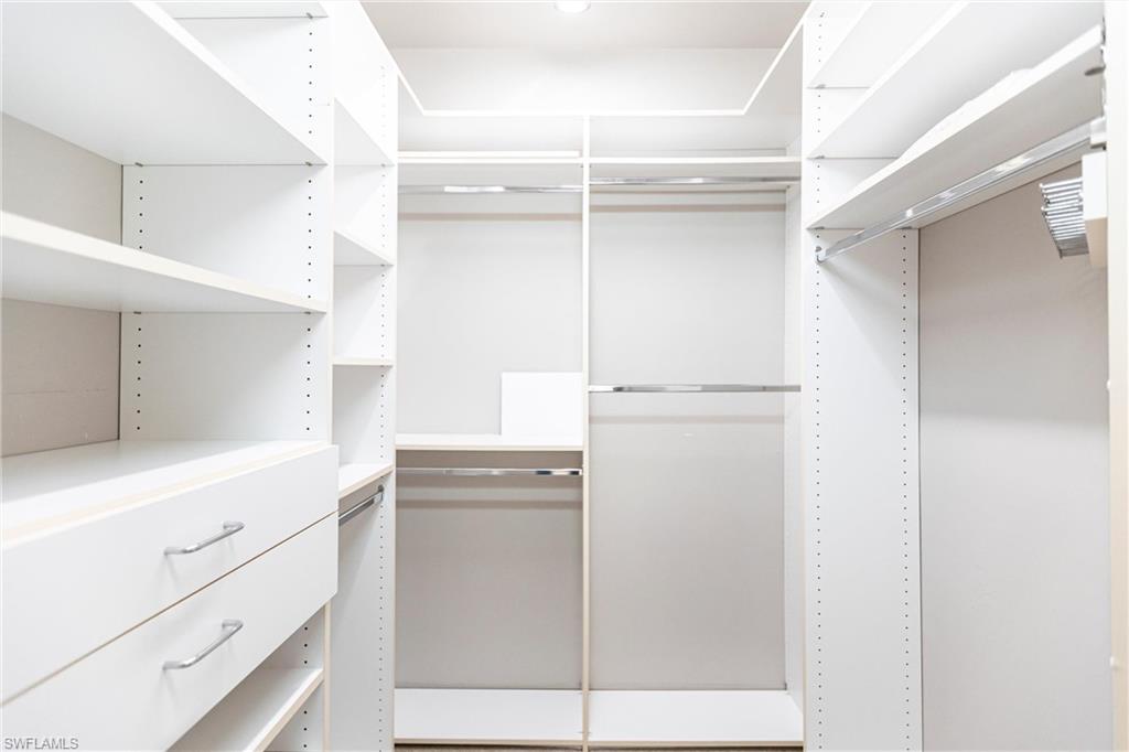 View of spacious custom (Closets-by-Design) neutral carpeted closet with two drawers and adjustable shelving and racks.