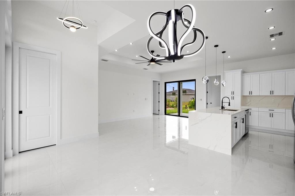 Open-concept living area featuring a modern kitchen island with waterfall countertop, white cabinetry with black hardware, and sleek pendant lighting