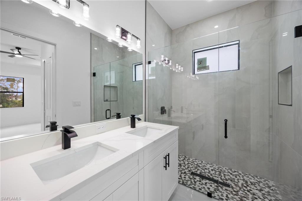 Contemporary bathroom featuring a dual vanity with white cabinetry and integrated sinks, matte black fixtures, and a frameless glass shower enclosure