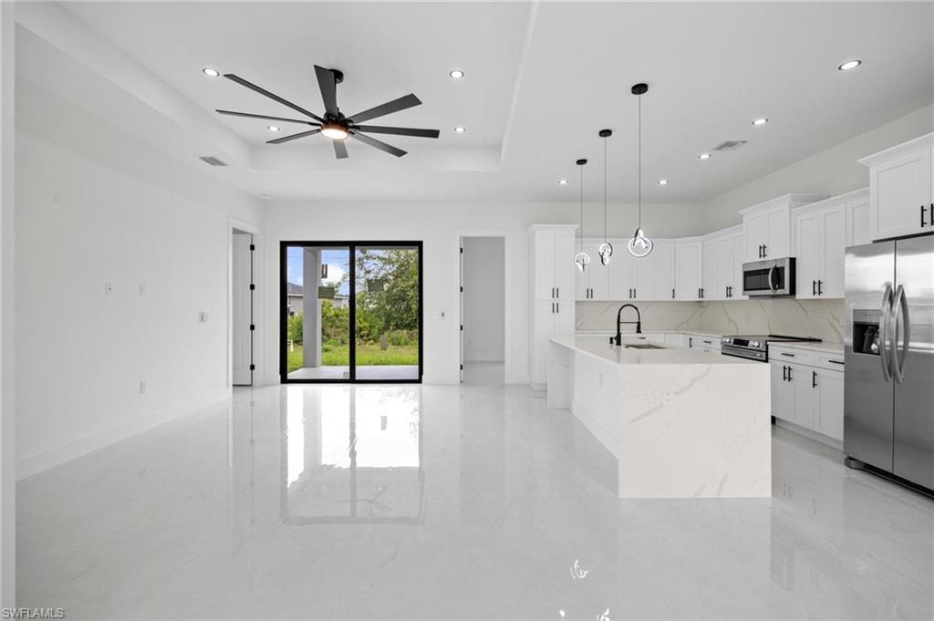 Open-concept living space featuring high-gloss tile flooring, a modern kitchen island with integrated sink, stainless steel appliances, and sleek white cabinetry