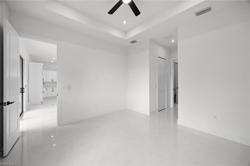 Spacious room featuring white tile flooring, white walls, a tray ceiling with recessed lighting, and a contemporary ceiling fan
