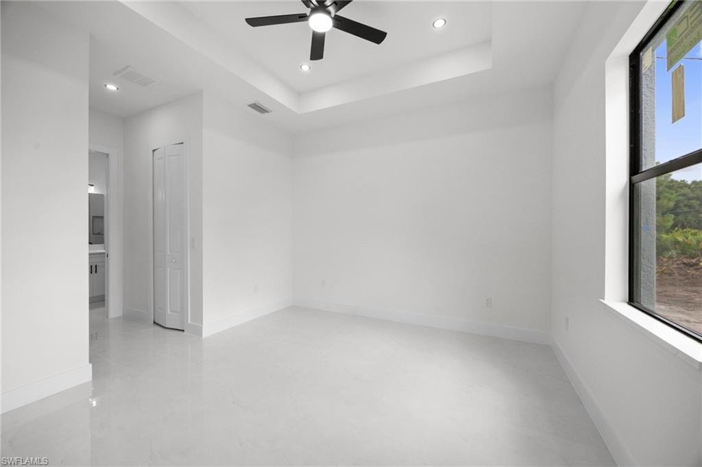 Spacious interior room featuring a tray ceiling with recessed lighting and a ceiling fan, large window, tile flooring, and clean white walls