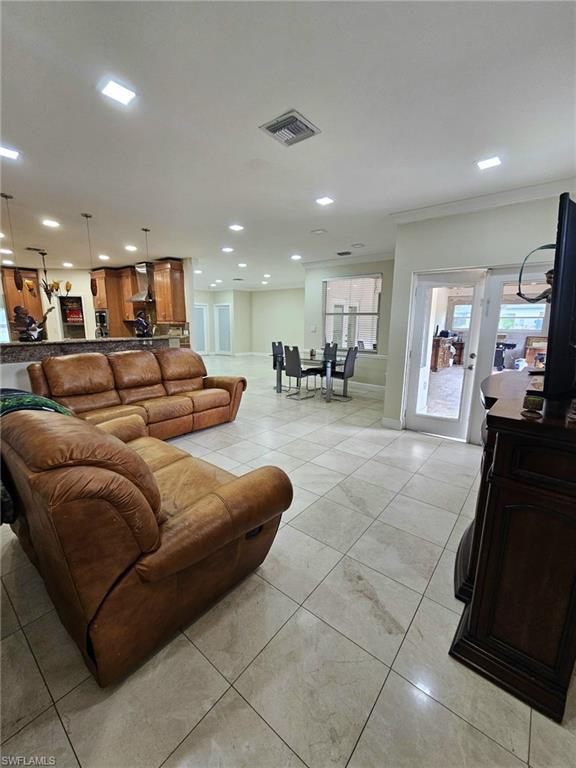 Open-concept living space featuring neutral tone tile flooring, recessed lighting, and crown molding