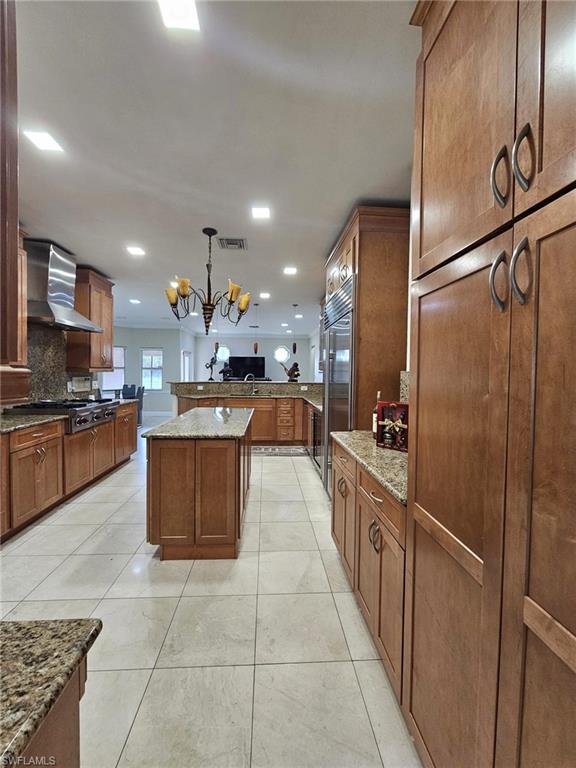 Expansive kitchen featuring light wood cabinetry, stone countertops, and large format tile flooring