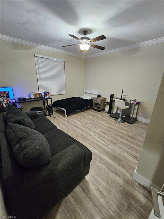Spacious room featuring wood-finish flooring, crown molding, a window with blinds, and a ceiling fan with integrated lighting