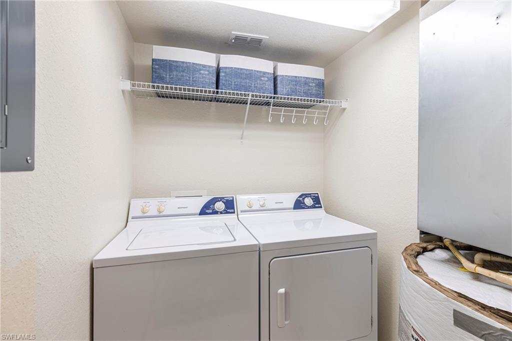 Washroom with washer and clothes dryer, electric panel, and a textured wall