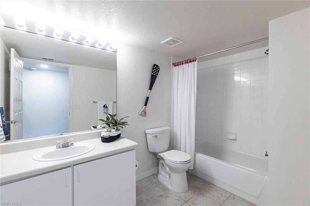 Bathroom featuring tile patterned floors, vanity, shower / tub combo, a textured ceiling, and a textured wall