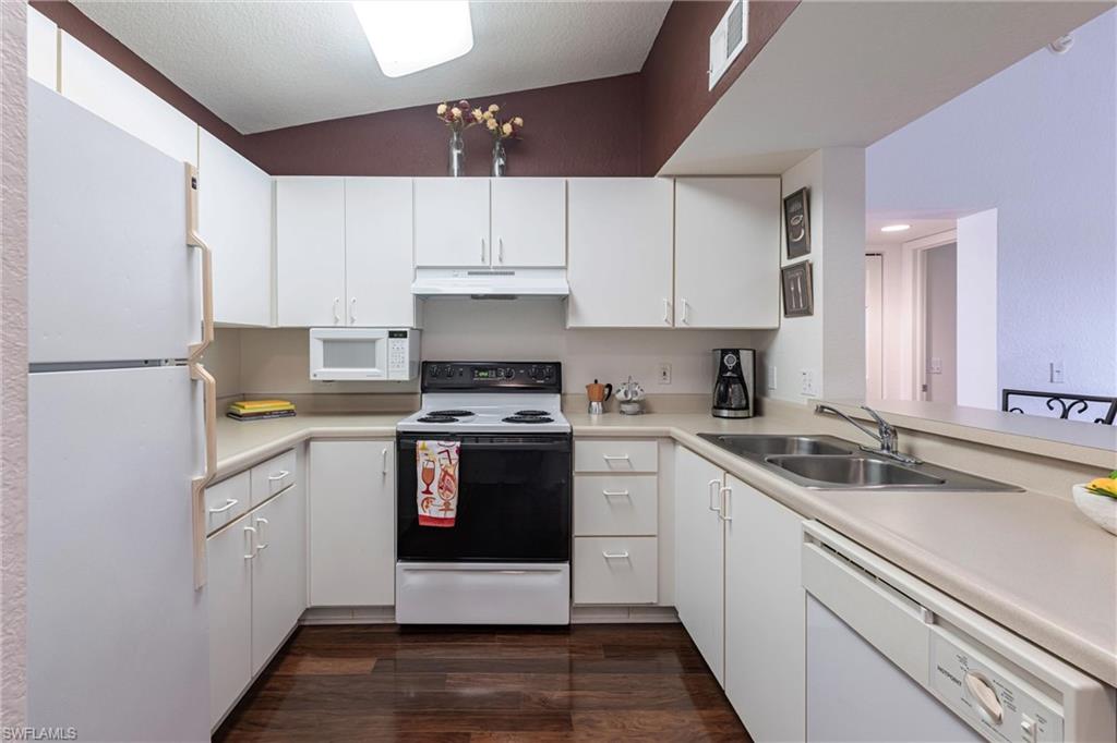Kitchen with white appliances, dark wood-type flooring, light countertops, white cabinets, and under cabinet range hood
