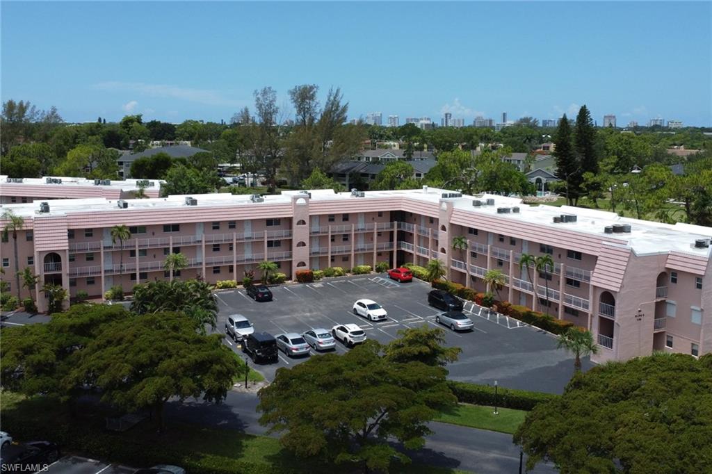 Multi-story residential building featuring private balconies, an exterior parking lot, and mature landscaping