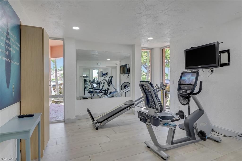 Fitness area featuring recessed lighting, a full-height mirrored wall, and light-toned tile flooring