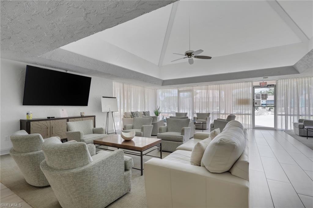 Spacious common area featuring a vaulted ceiling with a central ceiling fan, expansive window walls with sheer privacy treatments, and large format rectangular floor tiling