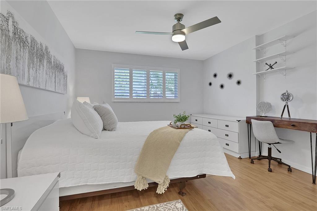 Bedroom featuring wood-finish flooring, a ceiling fan with integrated lighting, window shutters, built-in shelving, and a built-in dresser
