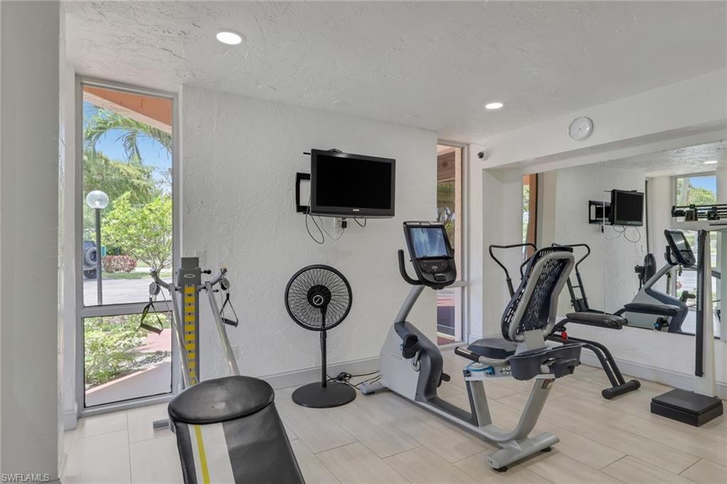 Dedicated fitness area featuring light-toned tile flooring, recessed lighting, expansive window panels, and a full-height wall mirror