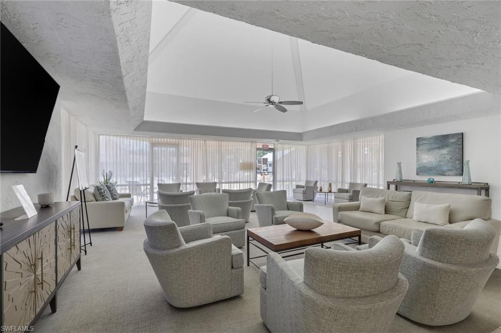 Spacious lounge area featuring a vaulted ceiling with ceiling fan, expansive window walls with sheer treatments, and abundant seating