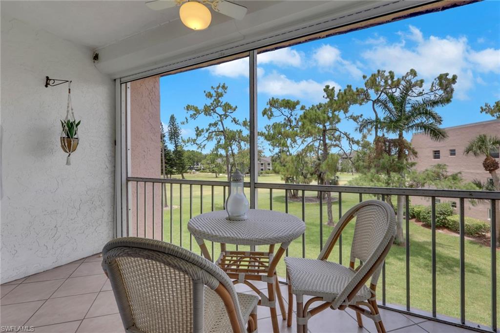 Screened patio featuring a ceiling fan, tiled flooring, and a railing overlooking a grassy area with mature trees