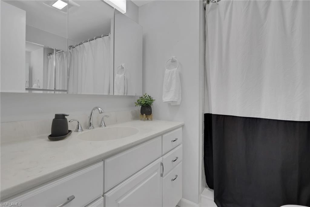 Bathroom vanity featuring a white countertop with an integrated sink, chrome faucet, white cabinetry, and an overhead mirrored medicine cabinet