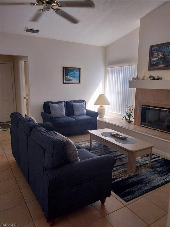 Living room with light tile patterned floors, a tiled fireplace, and ceiling fan