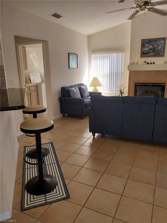Living room featuring a tile fireplace, light tile patterned floors, a ceiling fan, and lofted ceiling