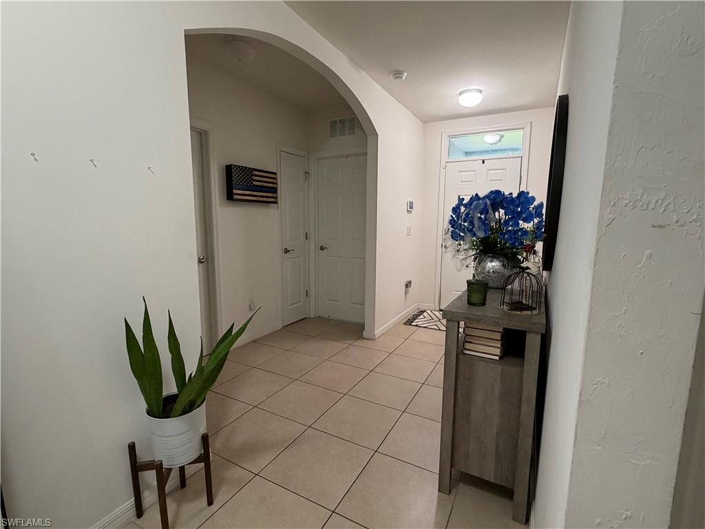 Entryway featuring neutral-toned tile flooring, an arched doorway, white interior doors, and a front entry door with a transom window