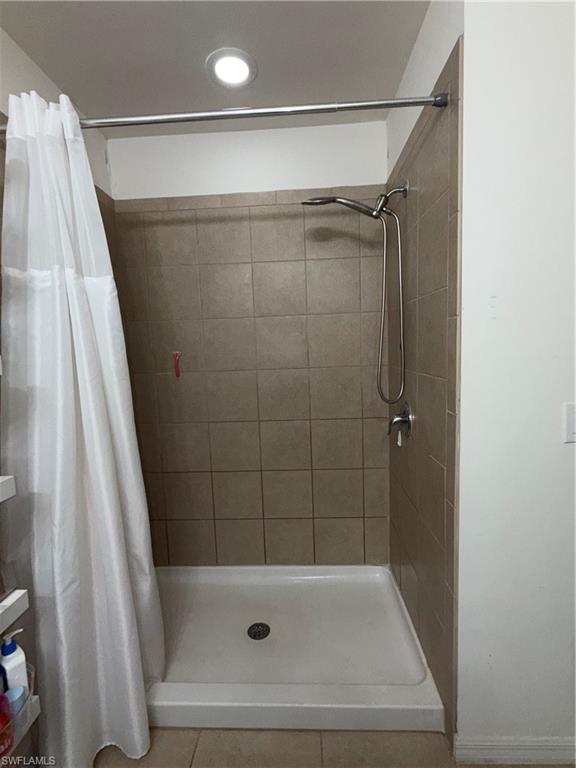 Shower stall with light-toned tiled walls, a white shower pan, and chrome fixtures