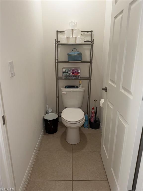 Compact powder room featuring a single toilet, neutral tile flooring, and white walls