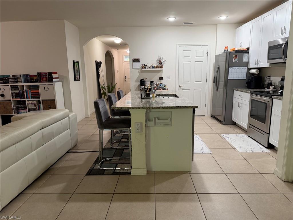 Kitchen with granite countertops, stainless steel appliances, white cabinetry, and tile flooring
