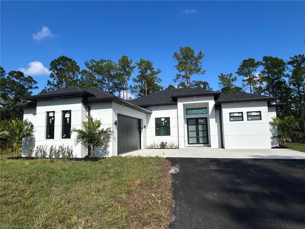 Prairie-style house with asphalt driveway, stucco siding, a front yard, a garage, and french doors