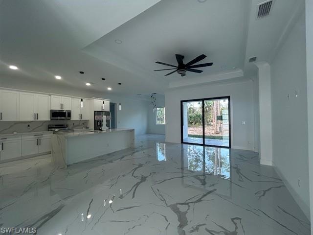 Living room featuring a raised ceiling, light marble finish floors, recessed lighting, and a ceiling fan