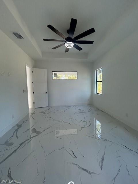 Spare room featuring light marble finish floors, a raised ceiling, and healthy amount of natural light