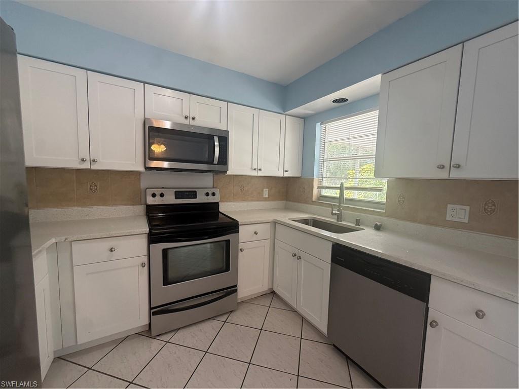 Kitchen featuring white cabinetry, stainless steel appliances, light-toned countertops, and a tiled backsplash with decorative accents