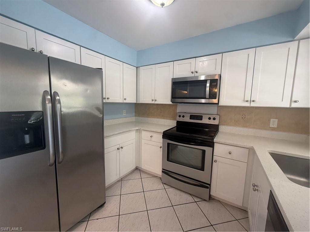Kitchen featuring white shaker cabinetry, stainless steel appliances, light-toned countertops, ceramic tile backsplash, and diagonal tile flooring