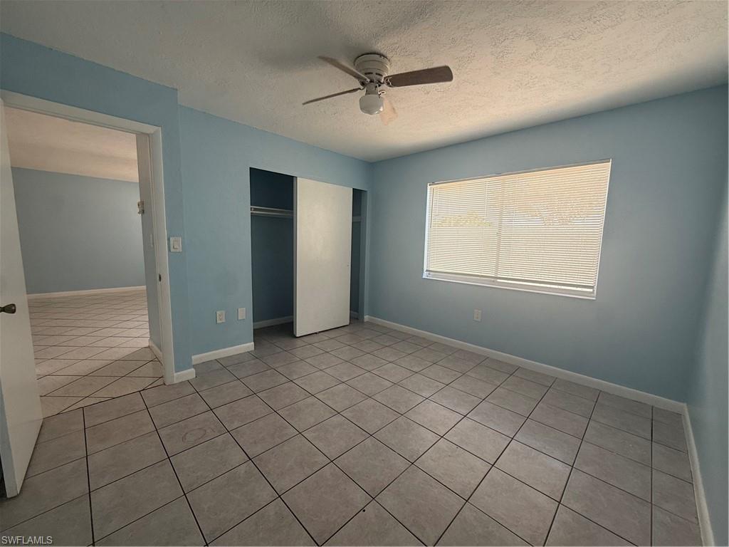 Room featuring light blue walls, gray tile flooring, a window with horizontal blinds, a ceiling fan, and an open closet with bi-fold doors