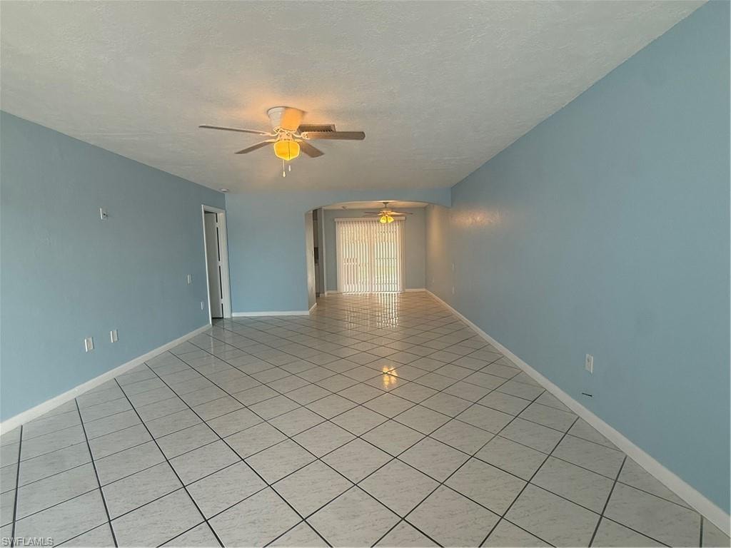 Expansive living area featuring light blue walls, white tiled flooring, and a ceiling fan with integrated lighting
