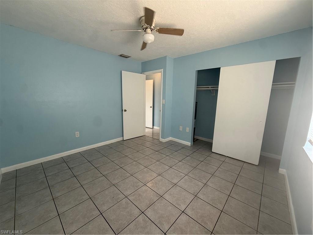 Tiled flooring extends throughout this room featuring a ceiling fan, a double-door closet with sliding panels, and a painted accent wall