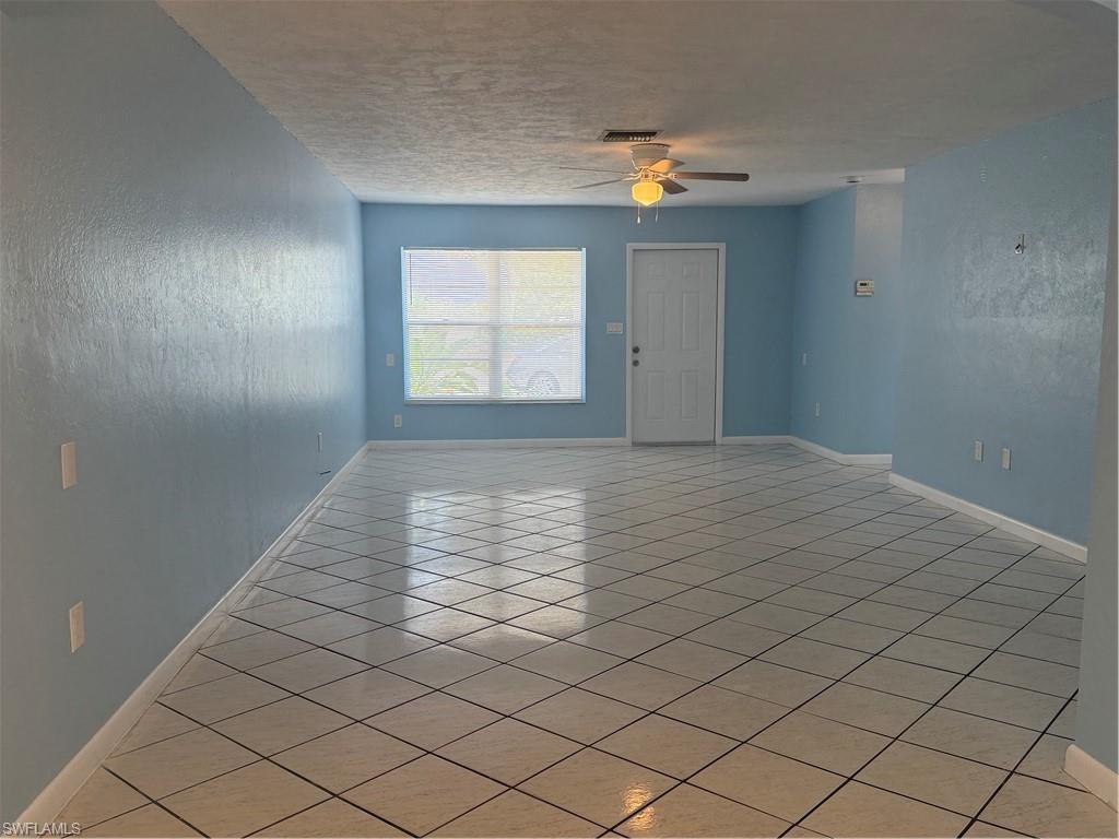 Spacious interior featuring light blue walls, a white ceiling fan with integrated lighting, a multi-pane window with horizontal blinds, a white paneled door, and diagonally laid tile flooring