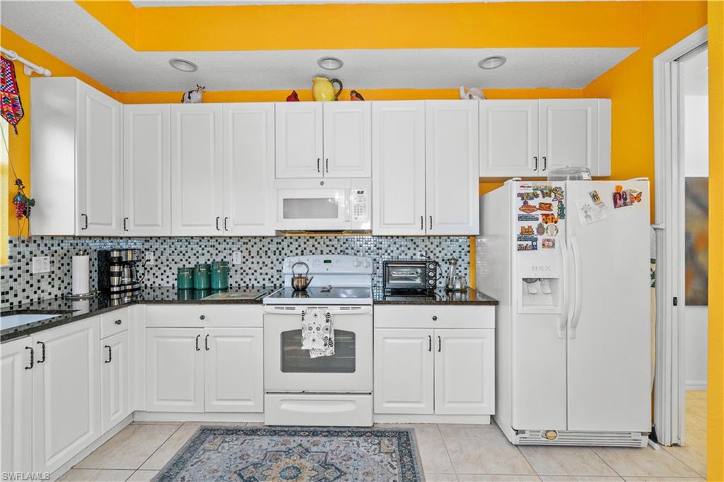 Kitchen with white appliances, white cabinetry, dark stone counters, decorative backsplash, and light tile patterned flooring