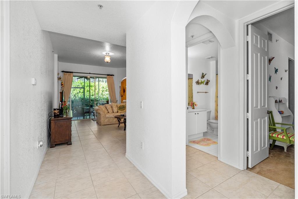 Hallway with arched walkways, light tile patterned floors, and a textured wall