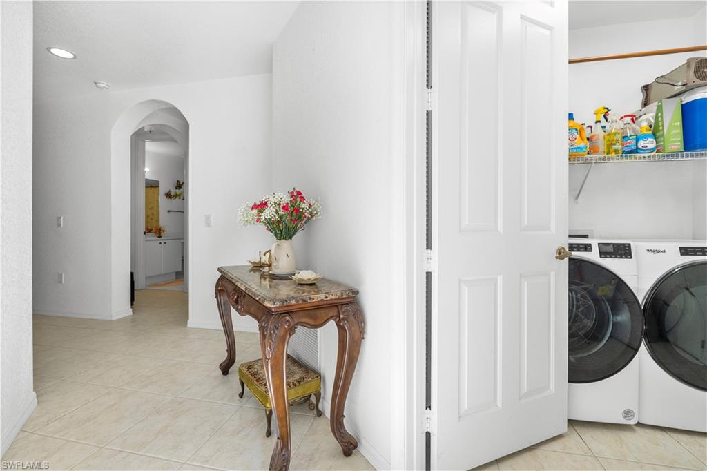 Washroom featuring arched walkways, light tile patterned floors, washing machine and clothes dryer, and recessed lighting