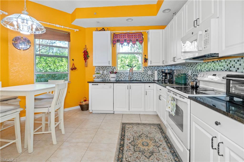 Kitchen with white appliances, white cabinetry, hanging light fixtures, dark stone countertops, and recessed lighting