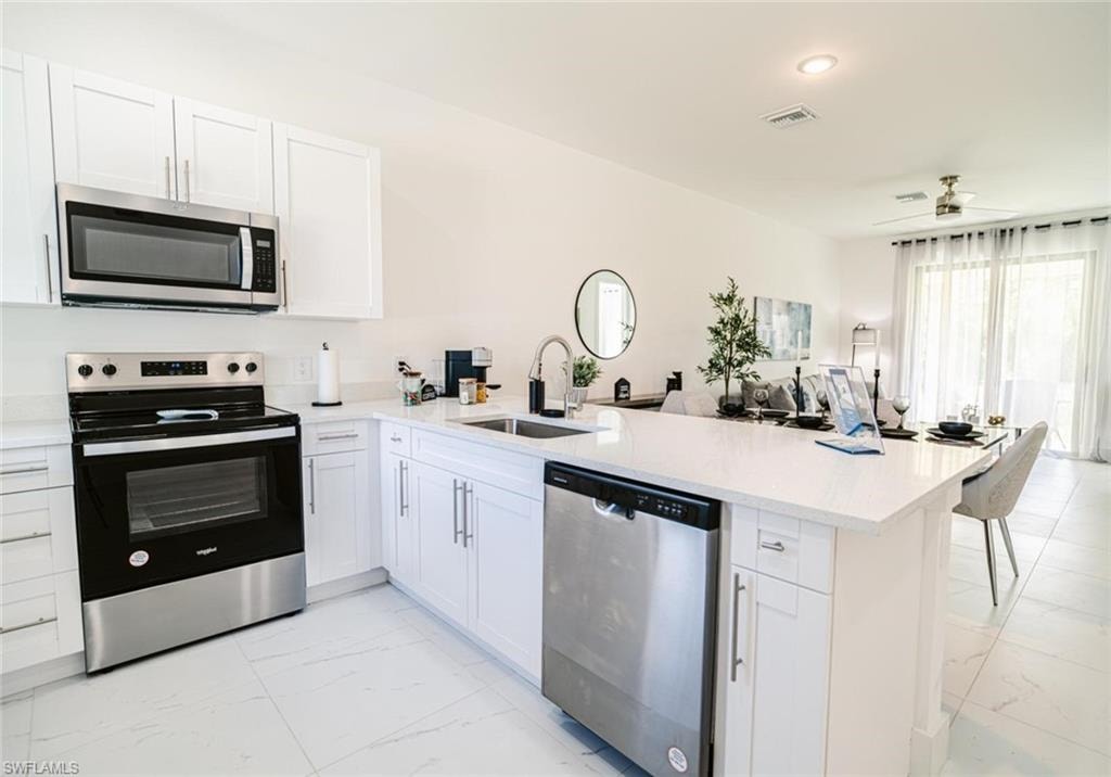 Modern kitchen featuring white cabinetry, stainless steel appliances, a white stone-finish countertop, and a built-in dishwasher