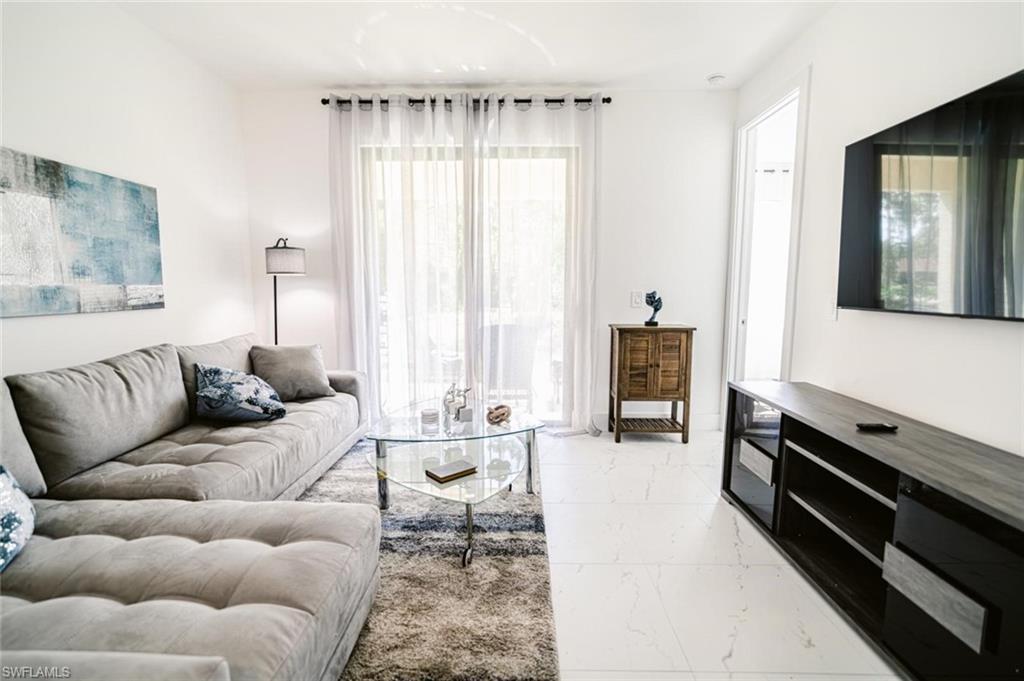 Bright living area featuring large format white tile flooring, a glass sliding door with sheer curtains, recessed lighting, and a wall-mounted television