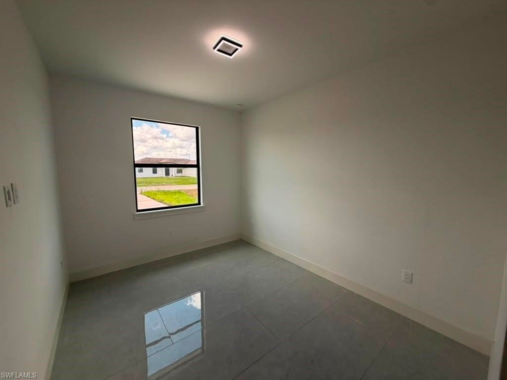 Neutral white walls featuring a single window with black trim, recessed ceiling lighting, and light grey tile flooring