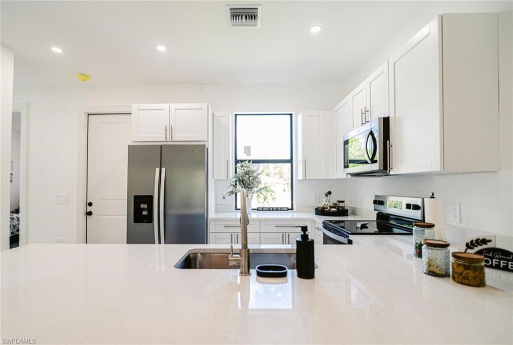 Modern kitchen featuring a white countertop island, stainless steel appliances, white cabinetry, and recessed lighting
