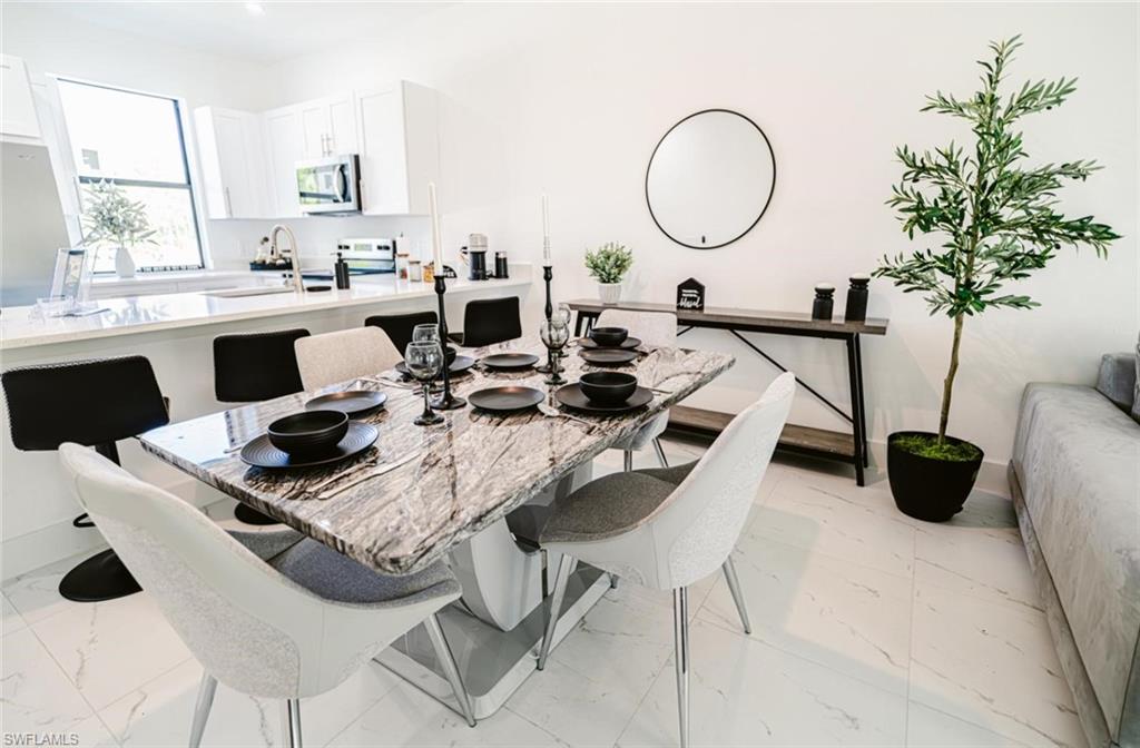 Open-concept dining area featuring a natural stone dining table, white tile flooring, and clean white walls
