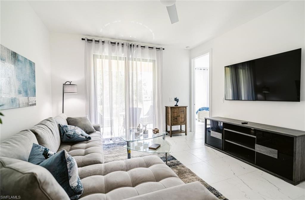 Bright living area featuring white walls, large sliding glass doors with sheer curtains, and light-toned tile flooring