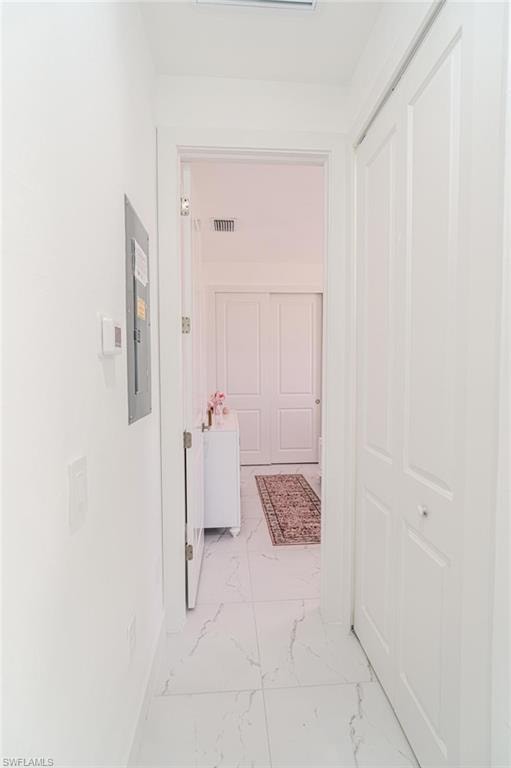 Hallway featuring white walls, white tile flooring with gray veining, and a closet with bifold doors