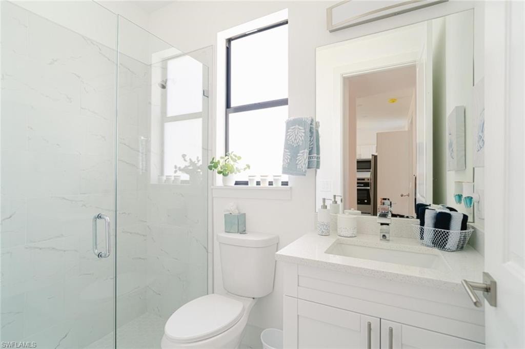 Bathroom featuring a glass-enclosed shower with white marble-patterned tile, a white vanity with an integrated sink and light-colored countertop, and a large wall-mounted mirror