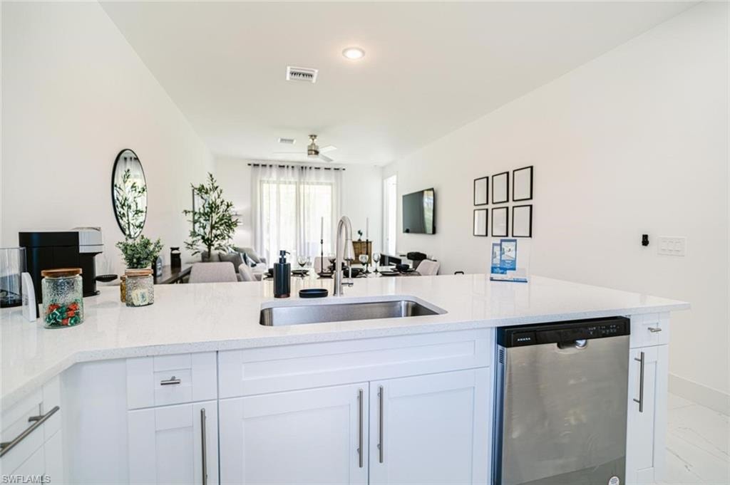 Kitchen island with a stainless steel undermount sink, a gooseneck faucet, white cabinetry, and a built-in stainless steel dishwasher