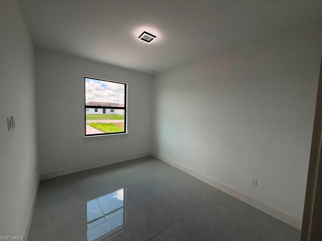Room with white walls, large window with black trim, square ceiling light fixture, and reflective grey tile flooring