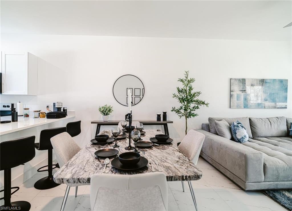 Open concept living area featuring a kitchen island with bar seating, white flat-panel cabinetry, a dining area with a marble-finish table, and tile flooring